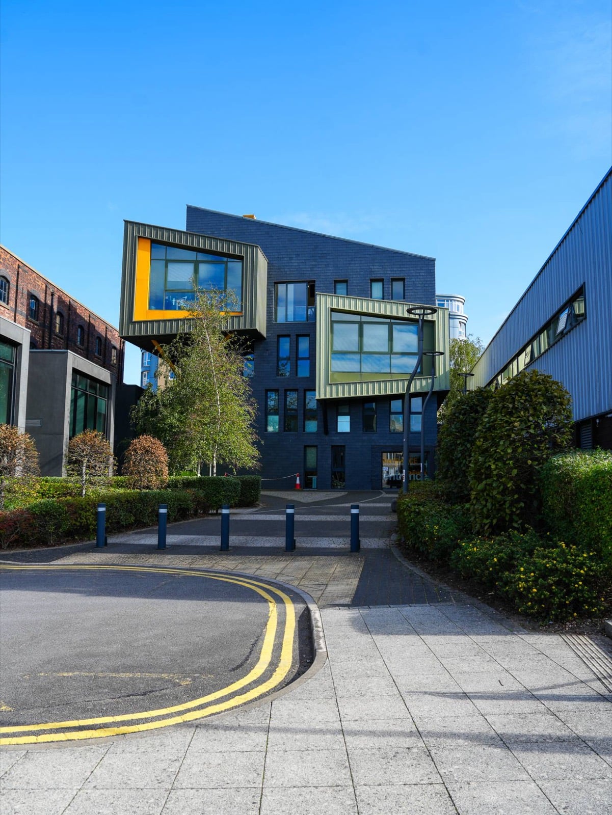 The Enterprise Building at the end of a tree-lined path, with its two cantilevered window boxes, one framed in yellow