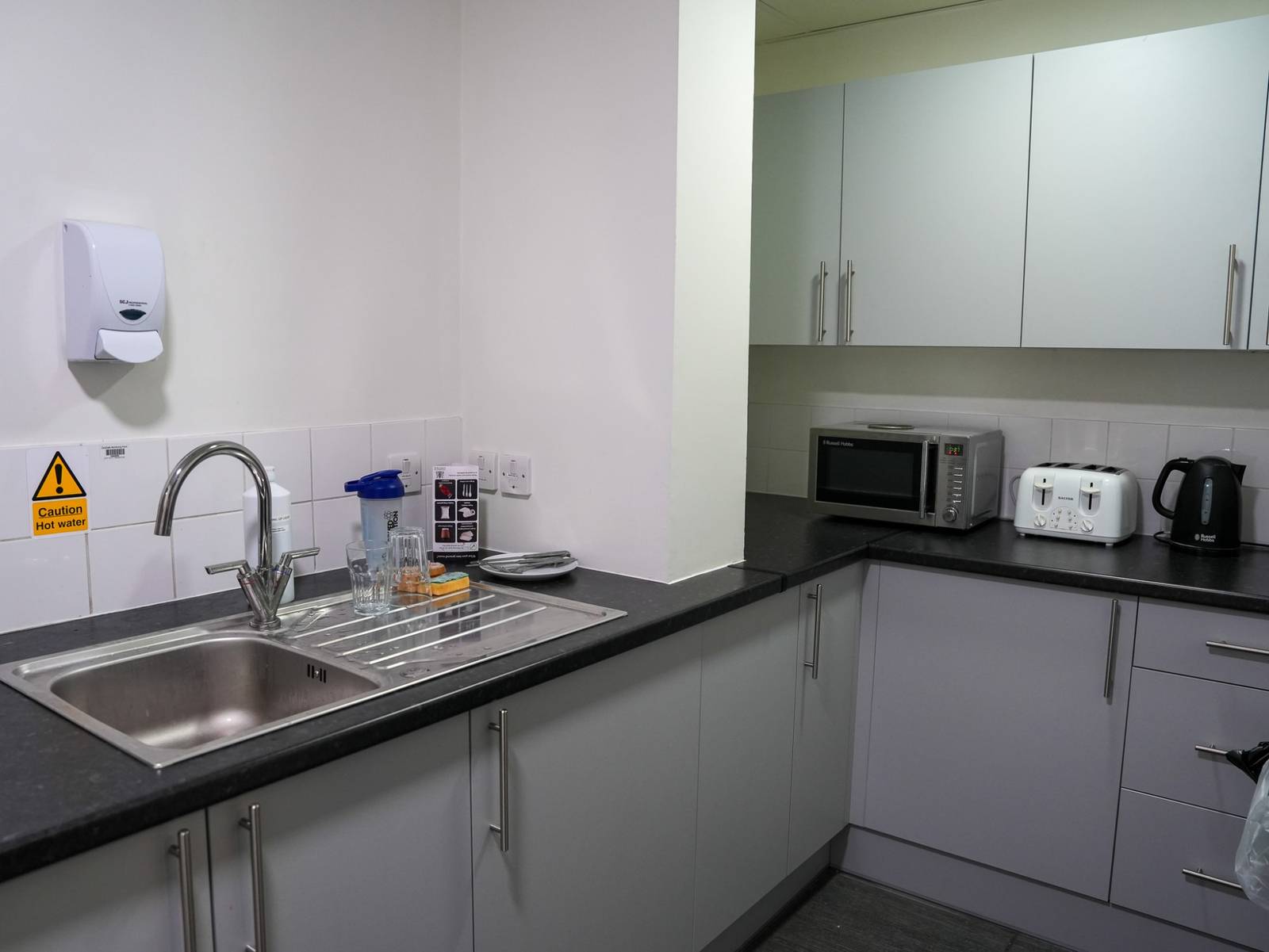 A shared kitchen with a sink, microwave, toaster and kettle along a run of grey units