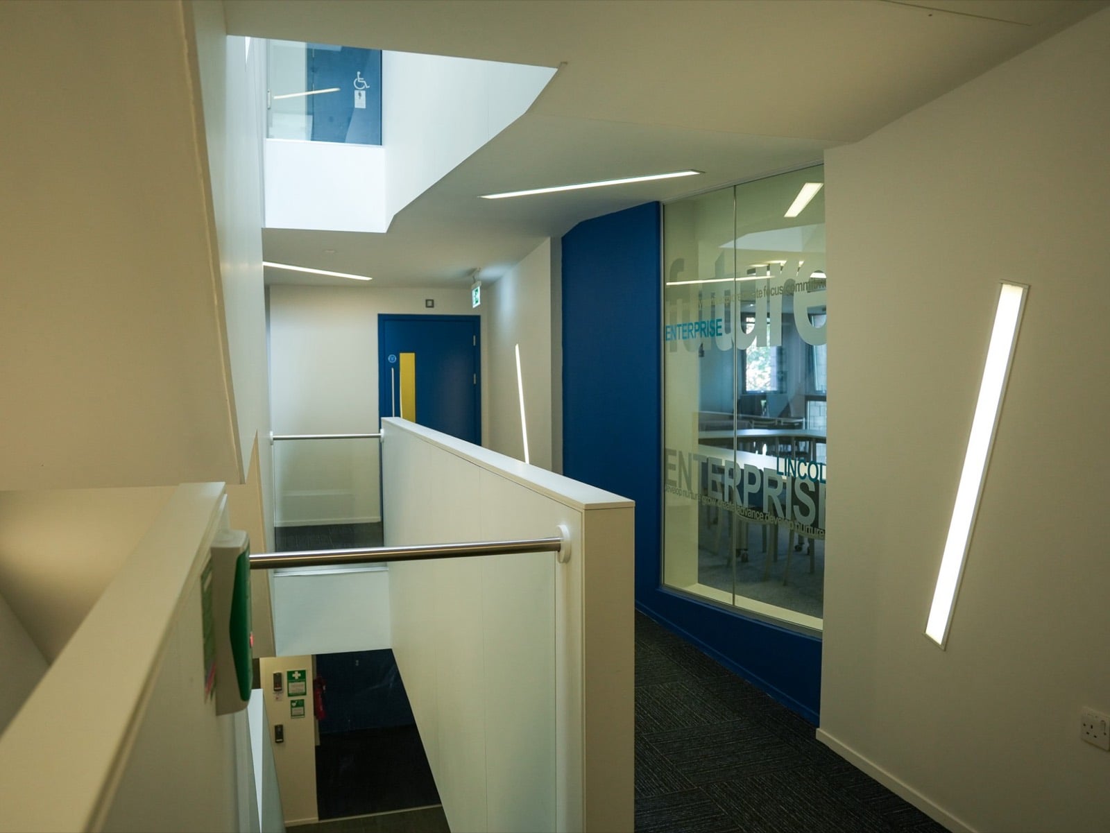 A bright stairwell landing beside a glass-walled meeting room etched with Lincoln Enterprise lettering