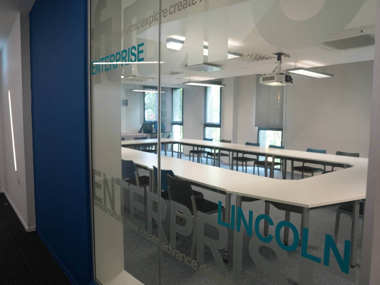 A meeting room seen through glass etched with Lincoln Enterprise, laid out in a hollow square under a projector