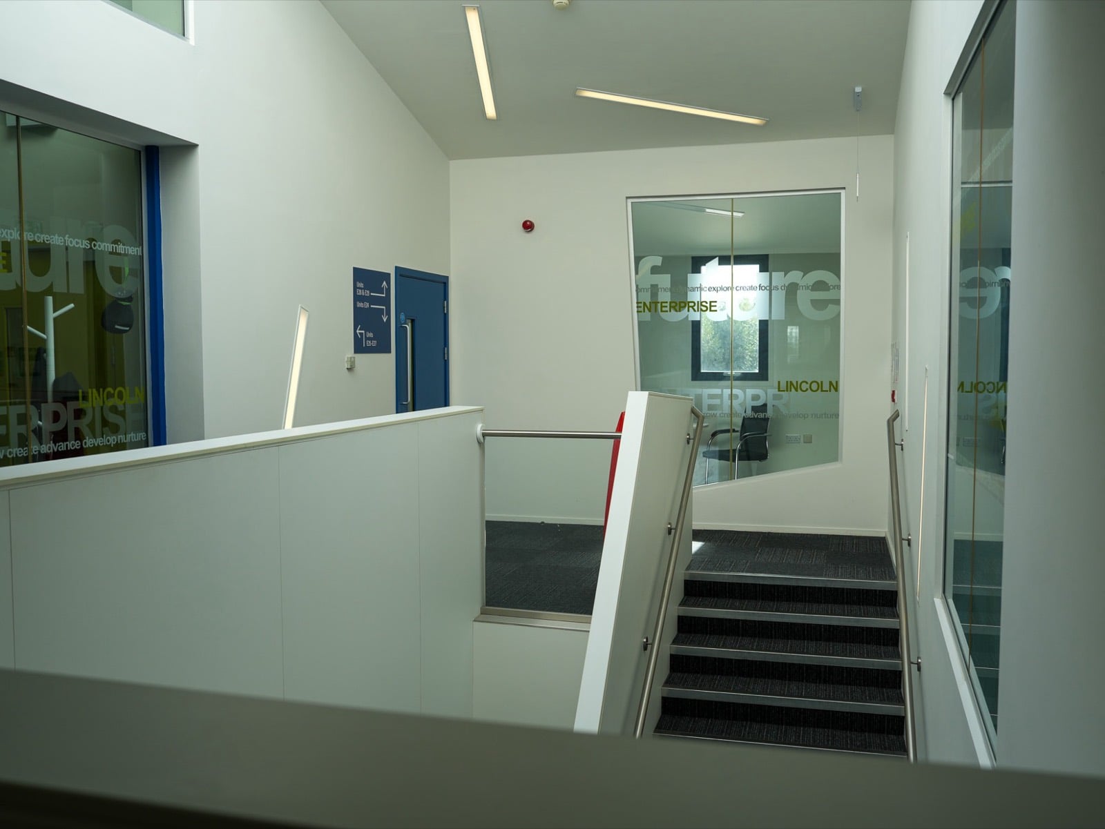 A short flight of stairs up to a landing, with glass-fronted offices and a sign pointing to the units