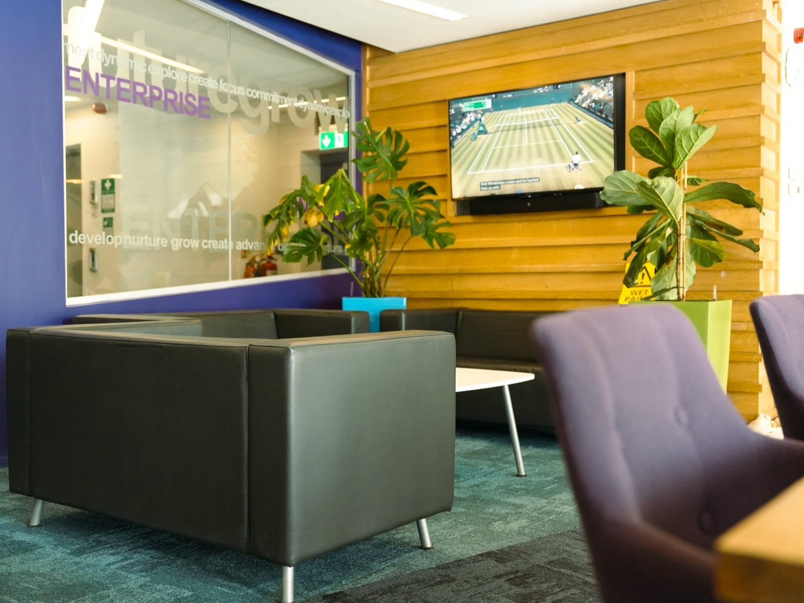 A breakout lounge with sofas and a wall-mounted screen, beside glass etched with the word Enterprise