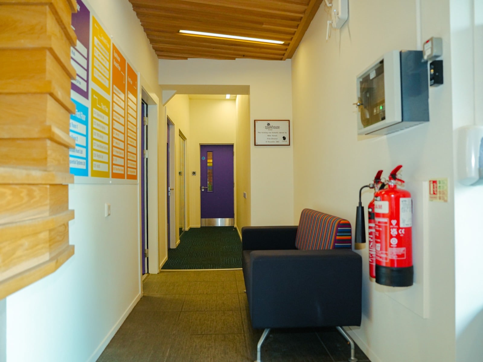 A Sparkhouse hallway with the tenant directory board, a seat and the 2003 opening plaque