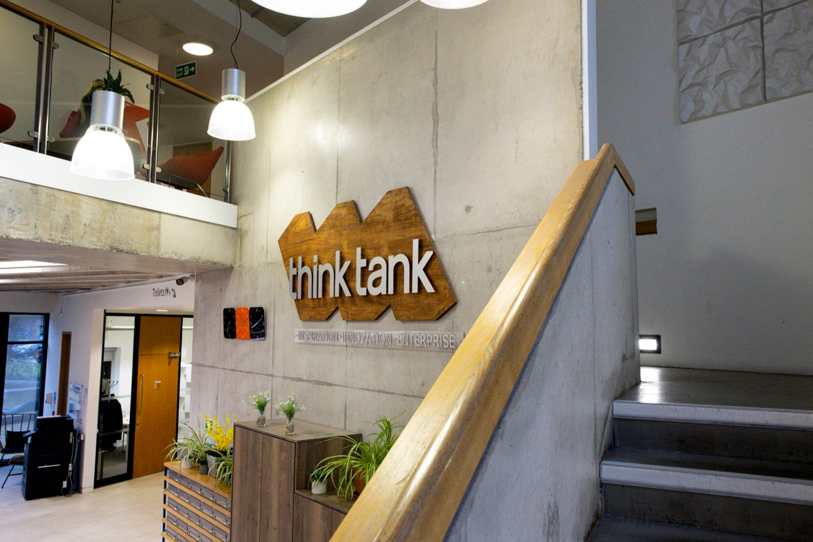 The Think Tank atrium, with the wooden think tank sign on a concrete wall beside the stairs and mezzanine