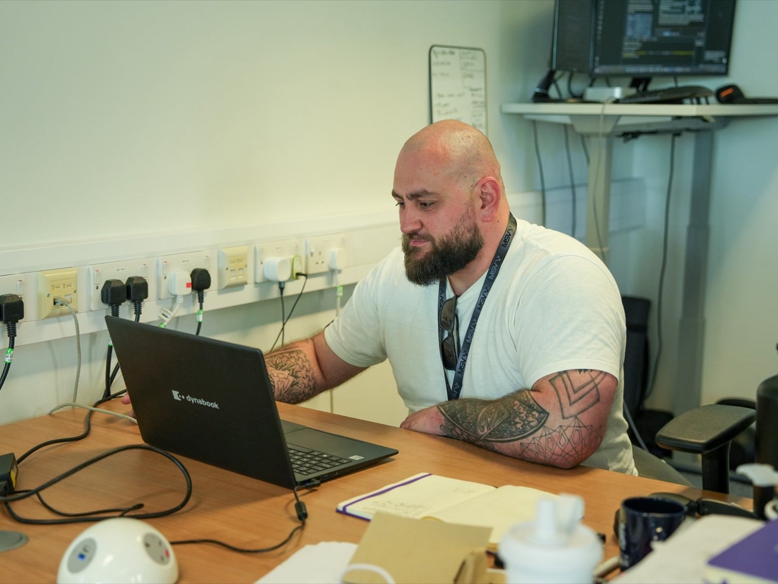 A founder working on a laptop at a desk, with a second screen and a whiteboard of notes behind