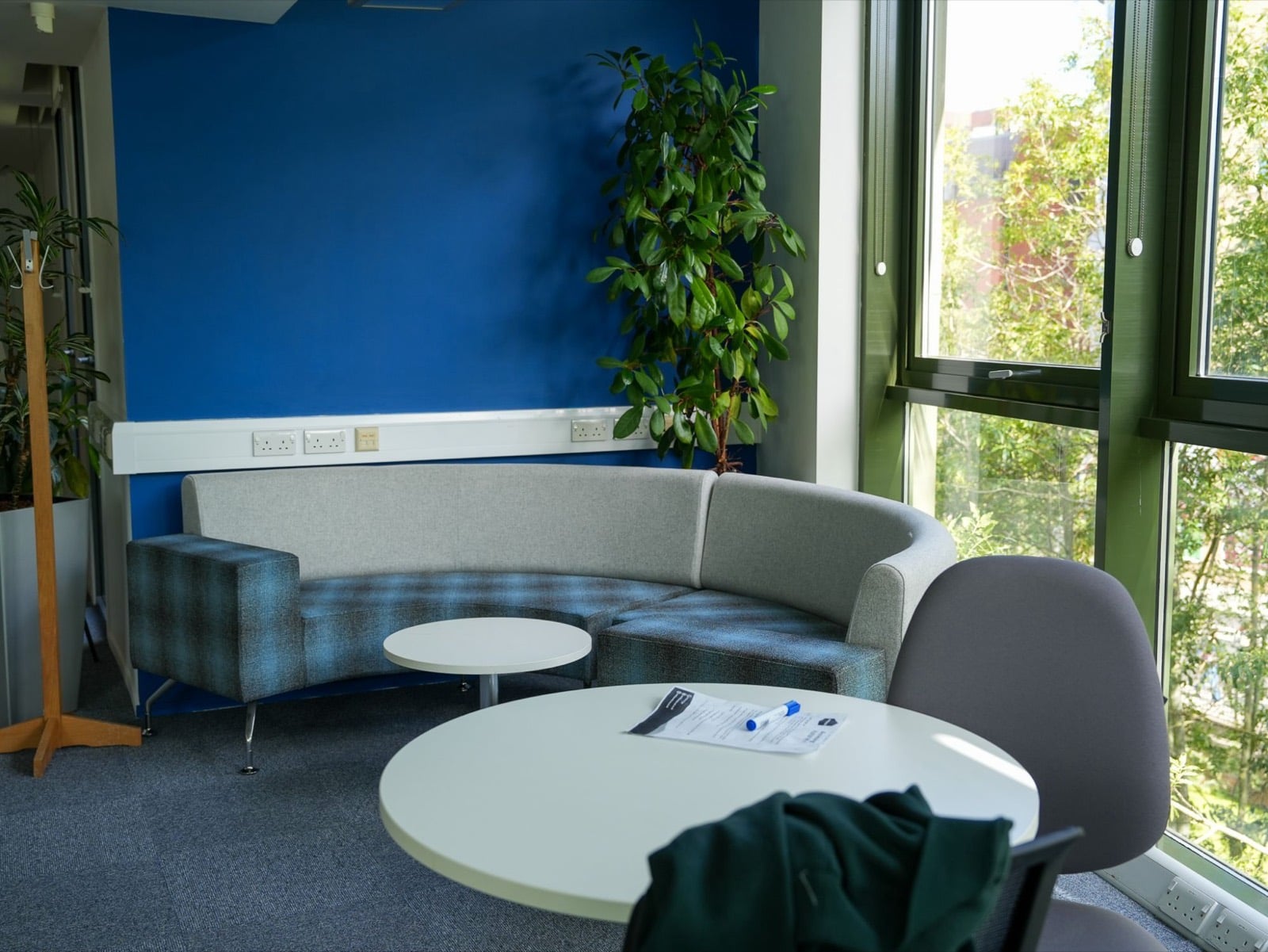 The curved sofa seen from a round meeting table by the windows, with a pen and papers on the table