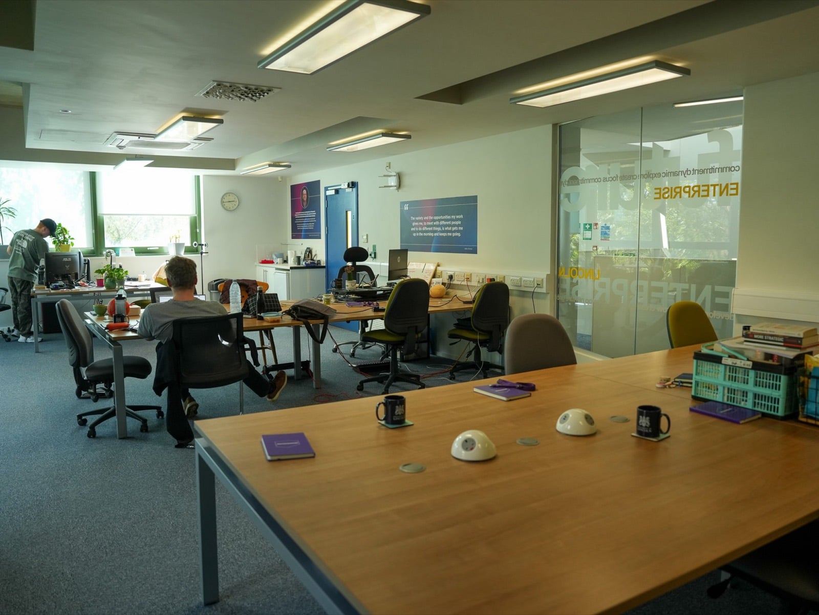 The Venture Lab open-plan floor, with people working at rows of desks beside a glass wall etched with Lincoln Enterprise