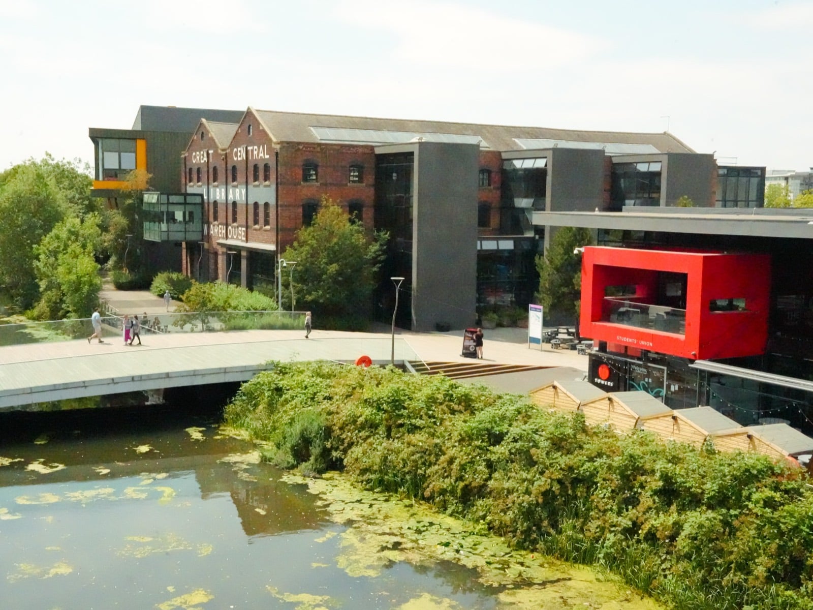 The University of Lincoln waterfront, with the Great Central Warehouse library across the bridge and people walking between the buildings