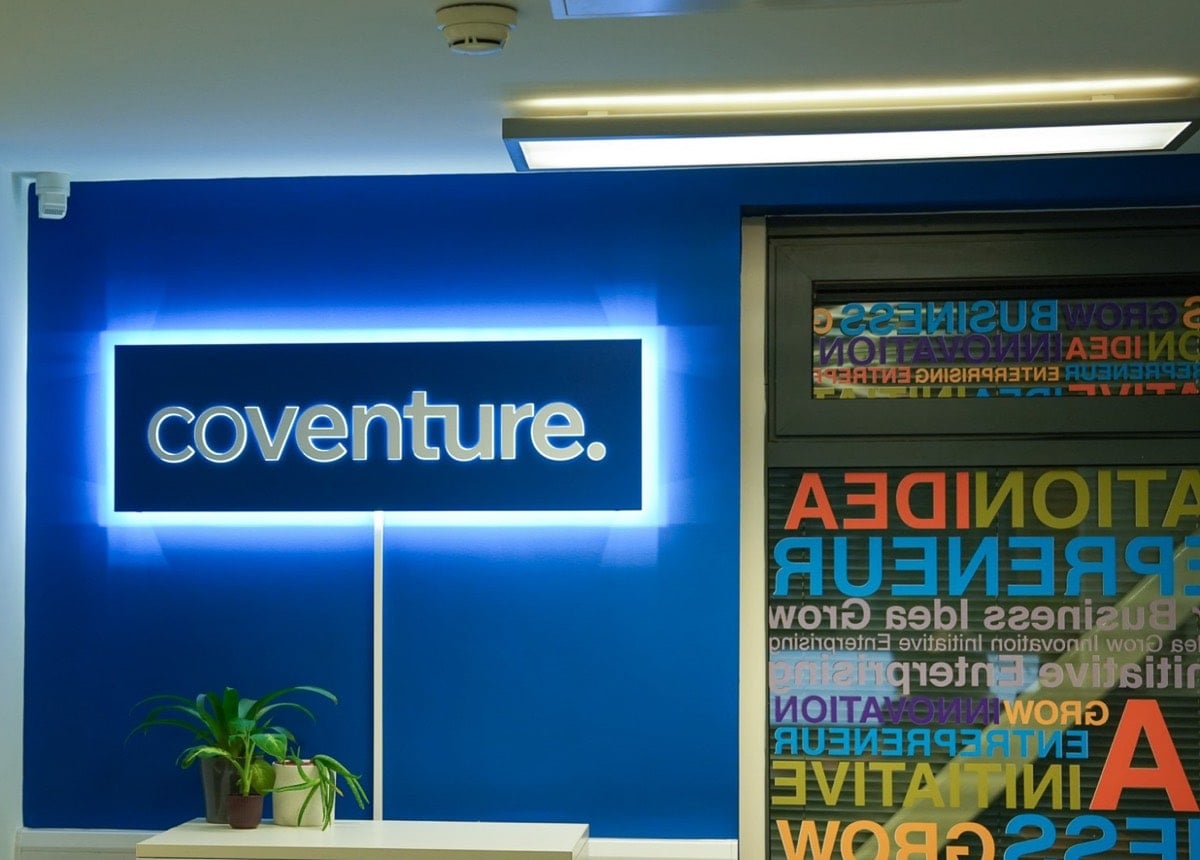 The illuminated Coventure sign on a blue wall at reception, beside a window graphic of enterprise words