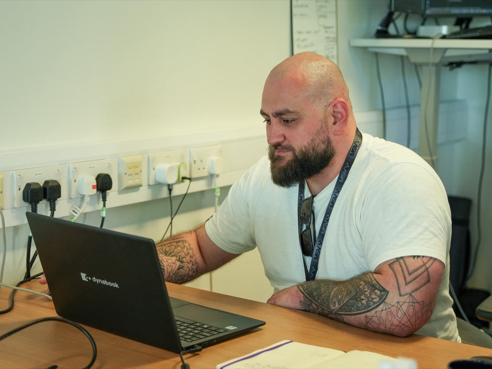 A founder working on a laptop at a desk, with a whiteboard of plans on the wall behind