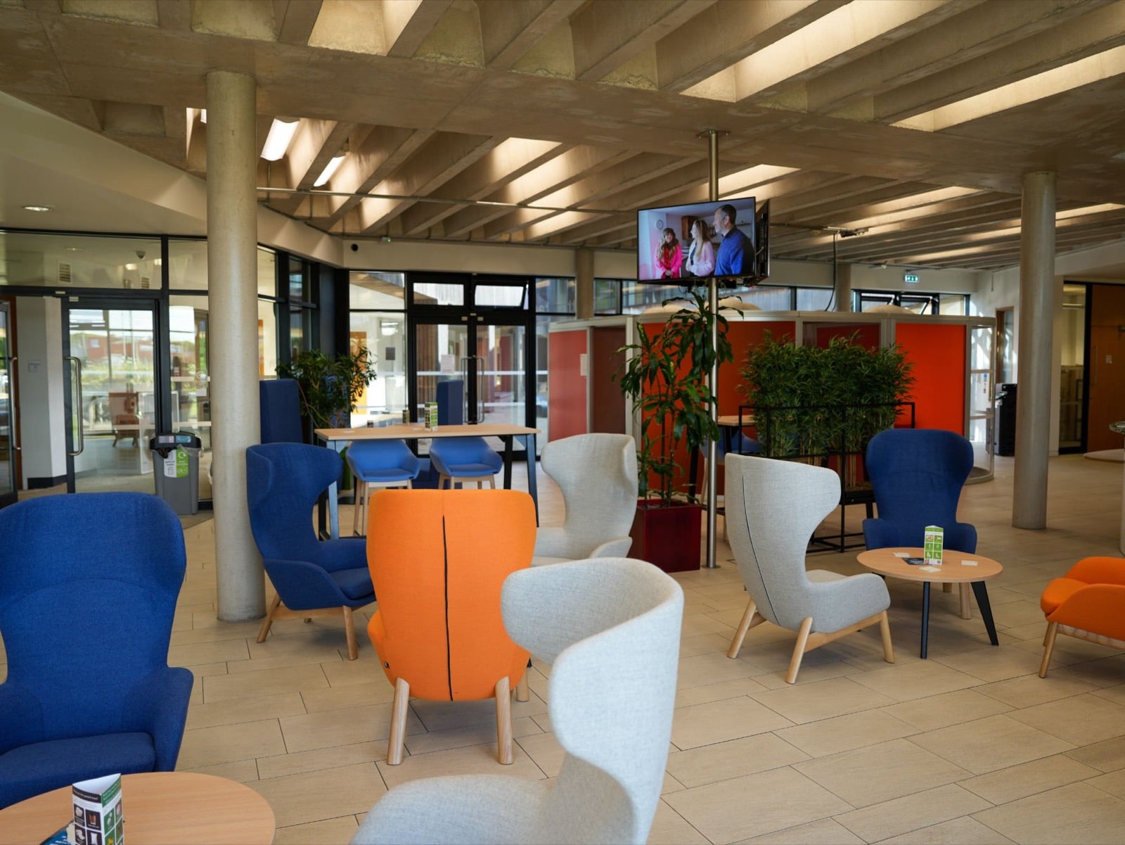The cafe lounge under an exposed concrete ceiling, with high-backed armchairs, poseur tables and planting