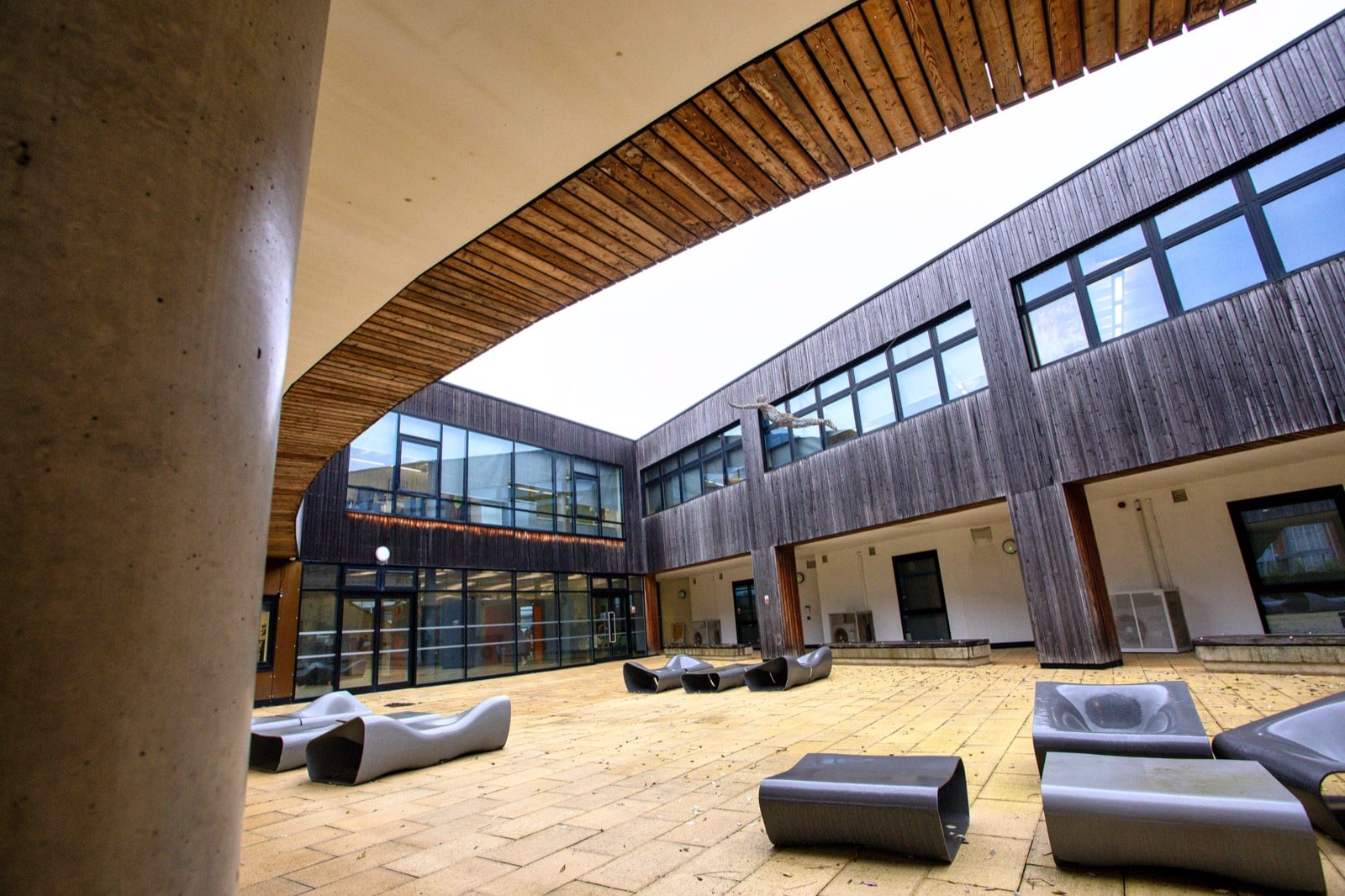 The Think Tank courtyard, a paved space with sculptural seating enclosed by timber-clad wings and a curved canopy