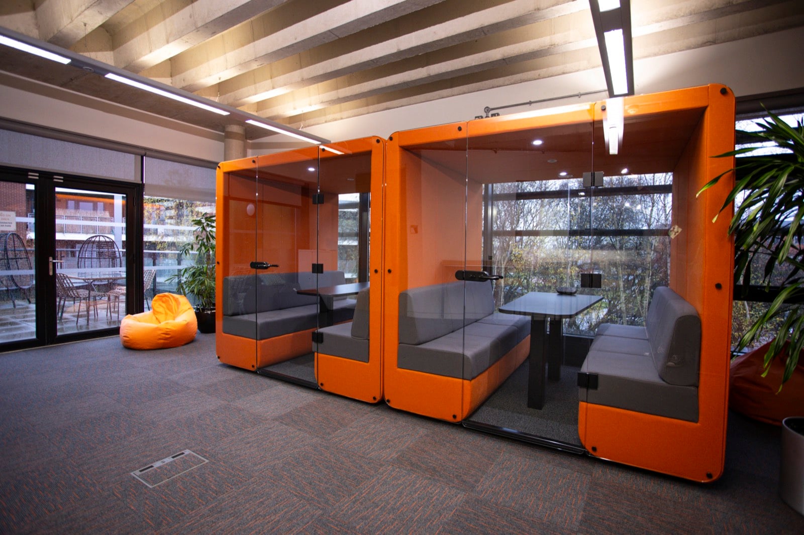 Two orange glazed meeting pods with bench seating, beside bean bags and doors onto a terrace