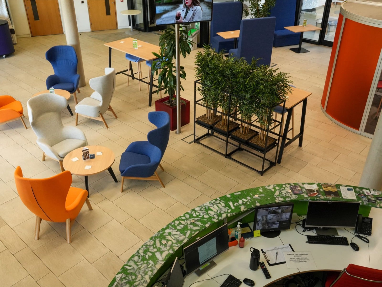 The lounge and curved reception desk seen from the floor above, with armchairs and bamboo planters