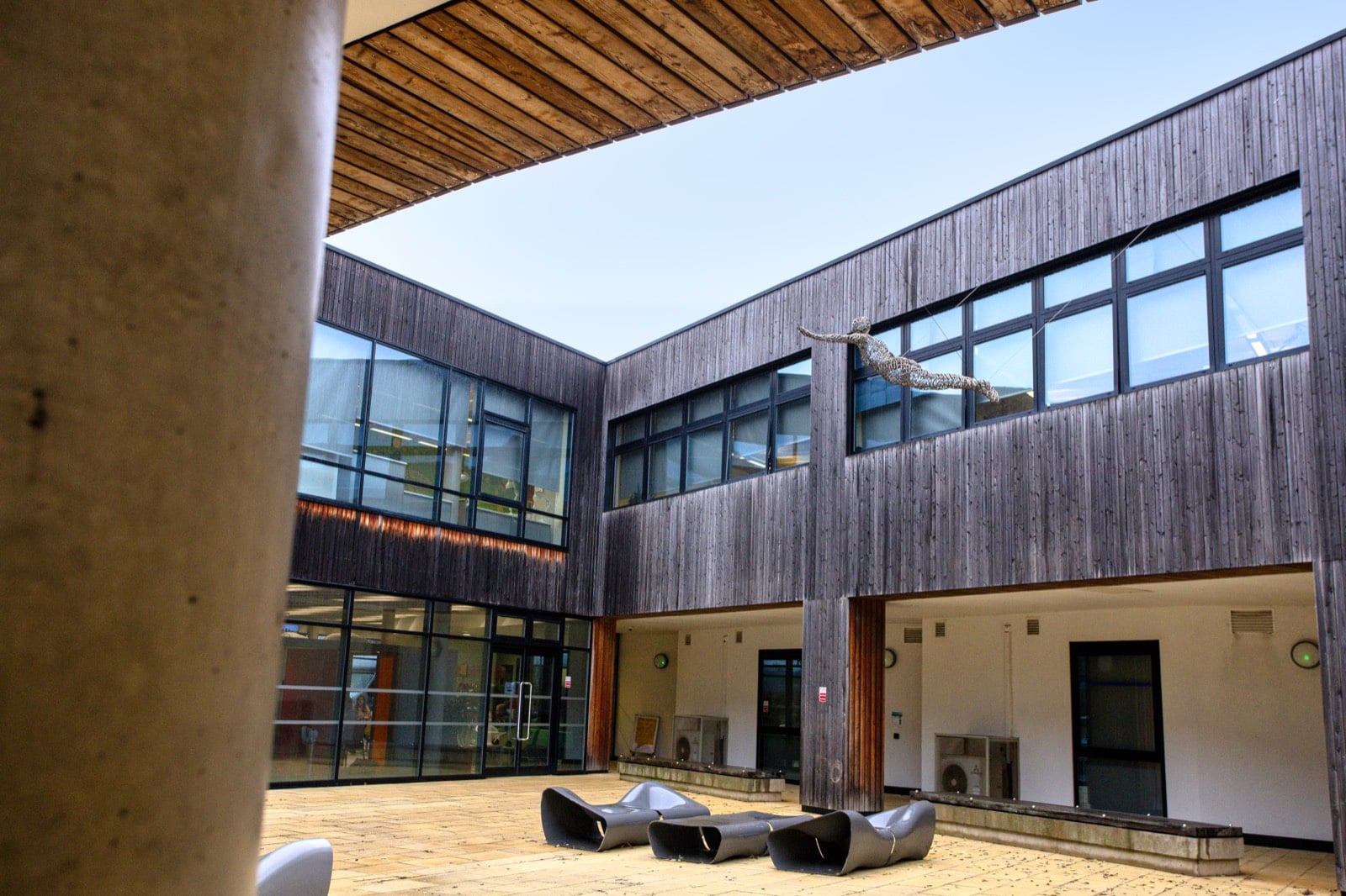 The Think Tank courtyard on a clear day, with a wire figure sculpture suspended above the timber-clad upper floor