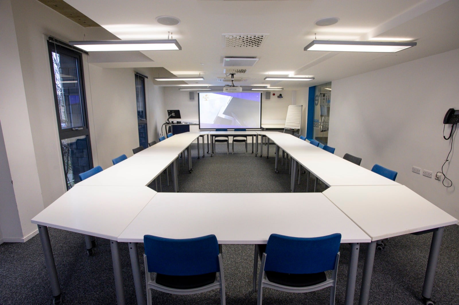 Meeting Room 1 laid out in a hollow square, facing a projector screen and whiteboard