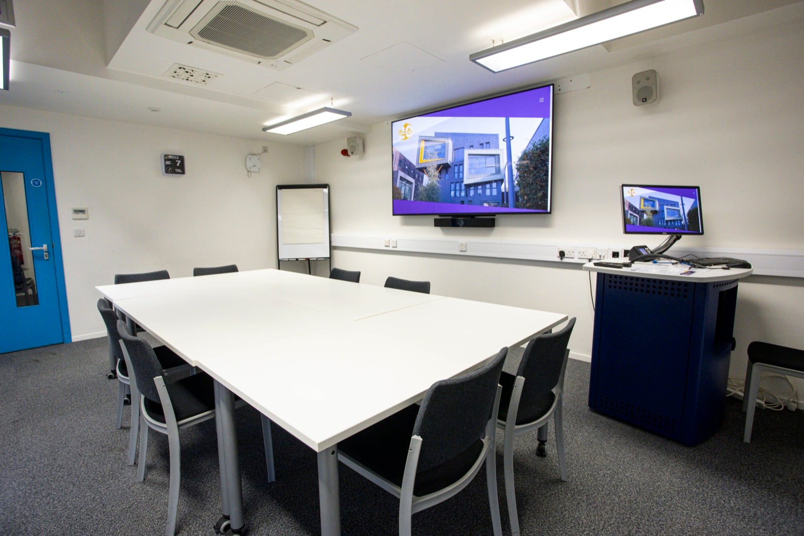 Meeting Room 2 set out boardroom style, with a wall-mounted screen, flipchart and presenting lectern
