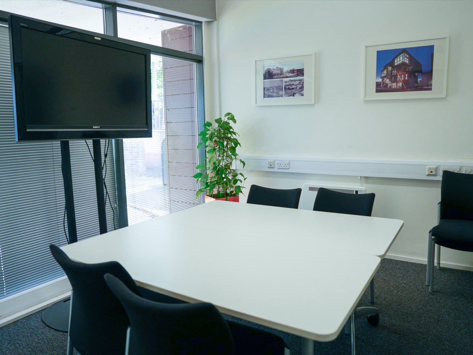 Meeting Room 3, a square table with six chairs by a window with blinds, and framed photographs of the Enterprise Building on the wall