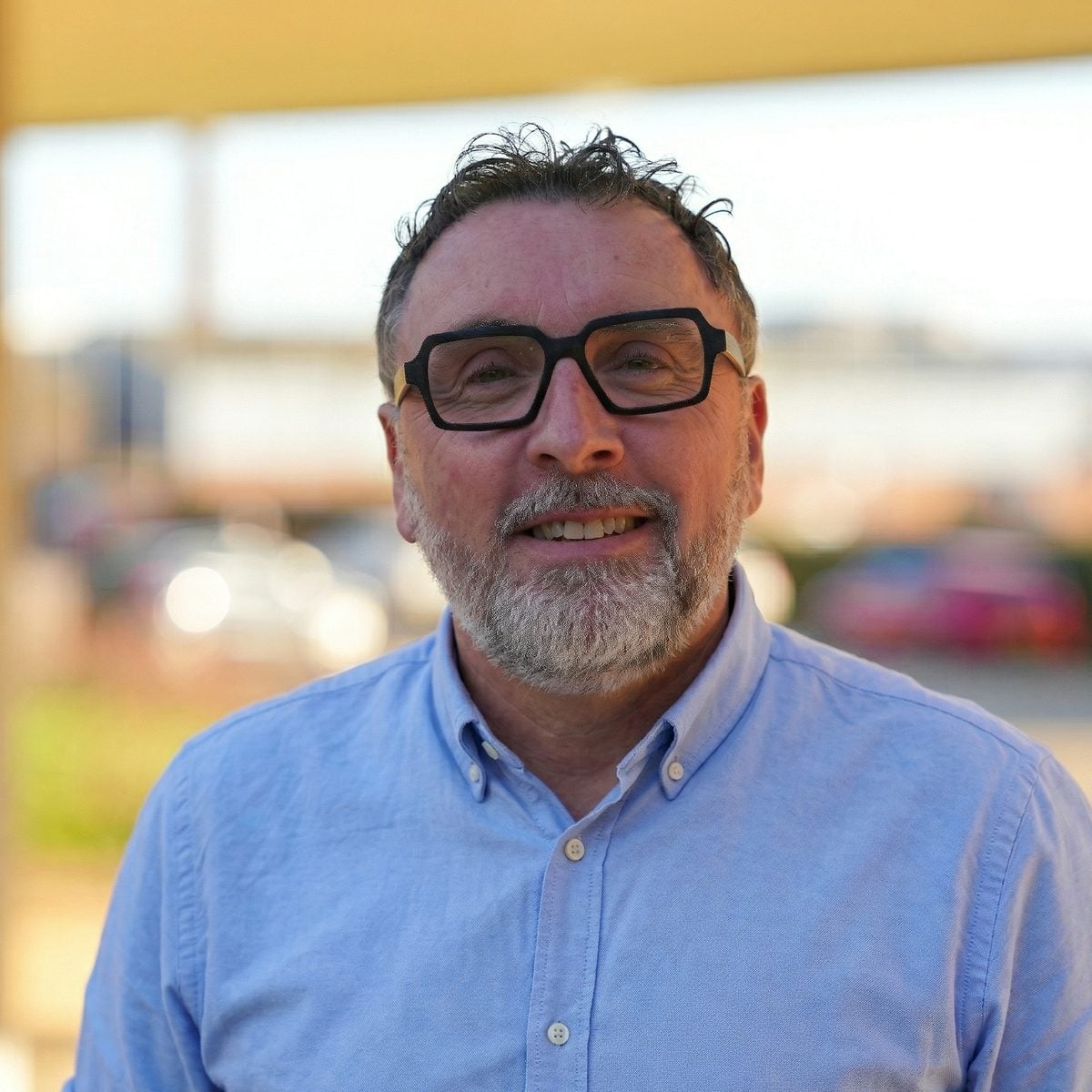 Craig Hutton of SMS Aero, smiling to camera outdoors in a blue shirt and dark-framed glasses